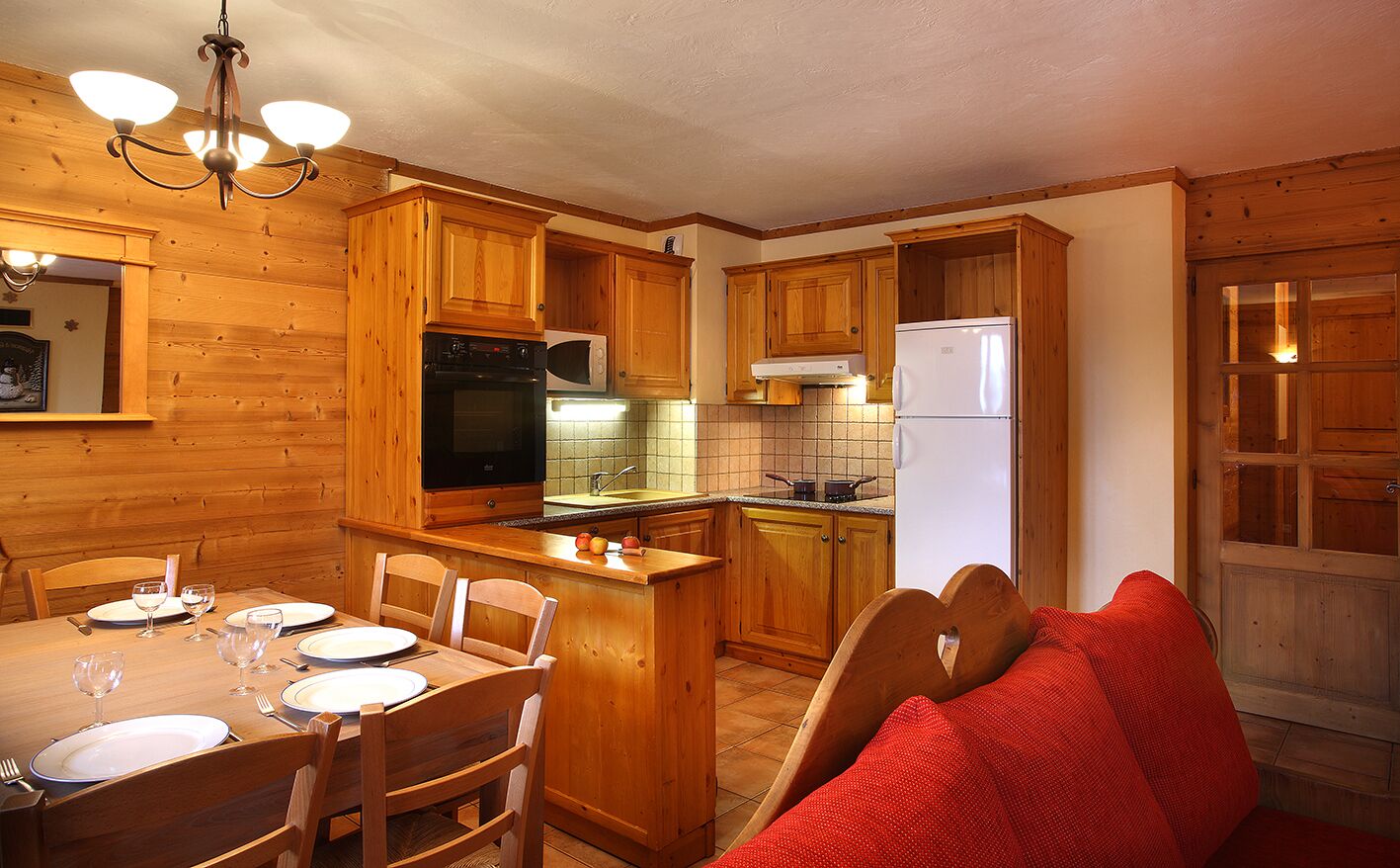 A wooden kitchen with a dining table set for four, a refrigerator, and a microwave.