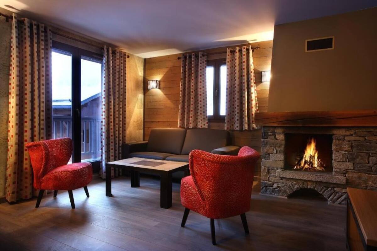 Une pièce chaleureuse avec une cheminée, un canapé, deux fauteuils rouges et une table.