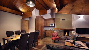 Une cuisine moderne avec des meubles en bois, une cheminée en pierre et un coin repas avec une table dressée pour quatre personnes.