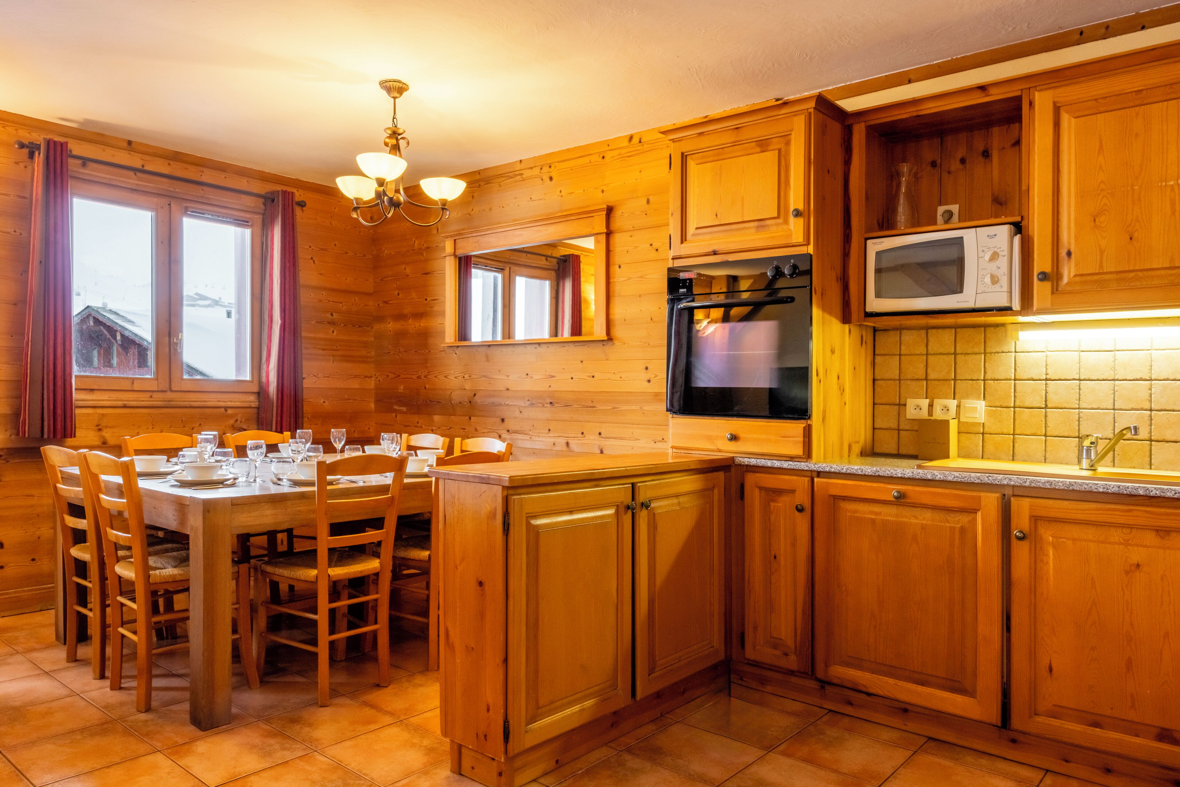 A wooden kitchen with a dining table set for four, a microwave, and a stove.