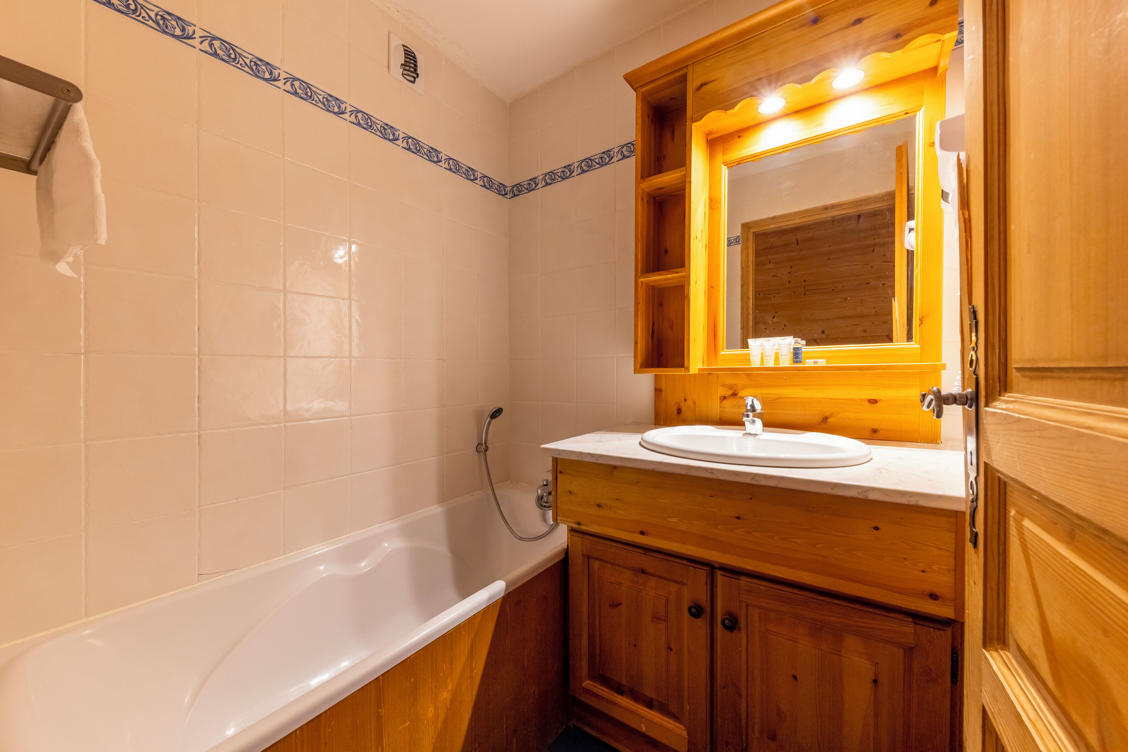 Un baño con una bañera blanca, armarios de madera y un espejo con marco de madera.