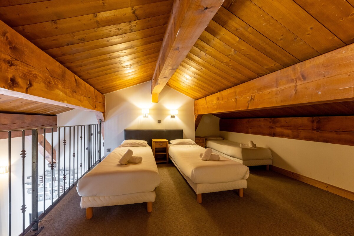 Une chambre confortable située sous les toits, avec deux lits simples, un plafond en bois et un balcon doté d’une rambarde en métal.