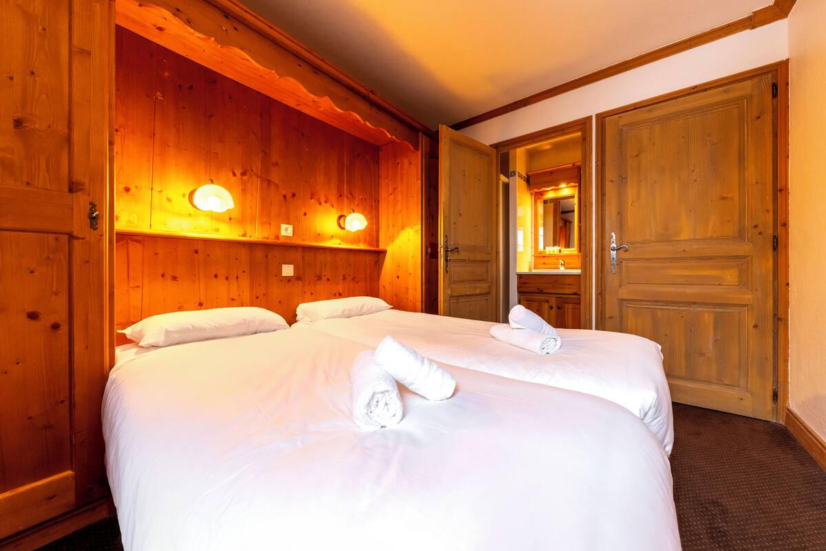 Une chambre d’hôtel avec des boiseries, deux lits avec du linge de lit blanc et un grand miroir dans un coin.