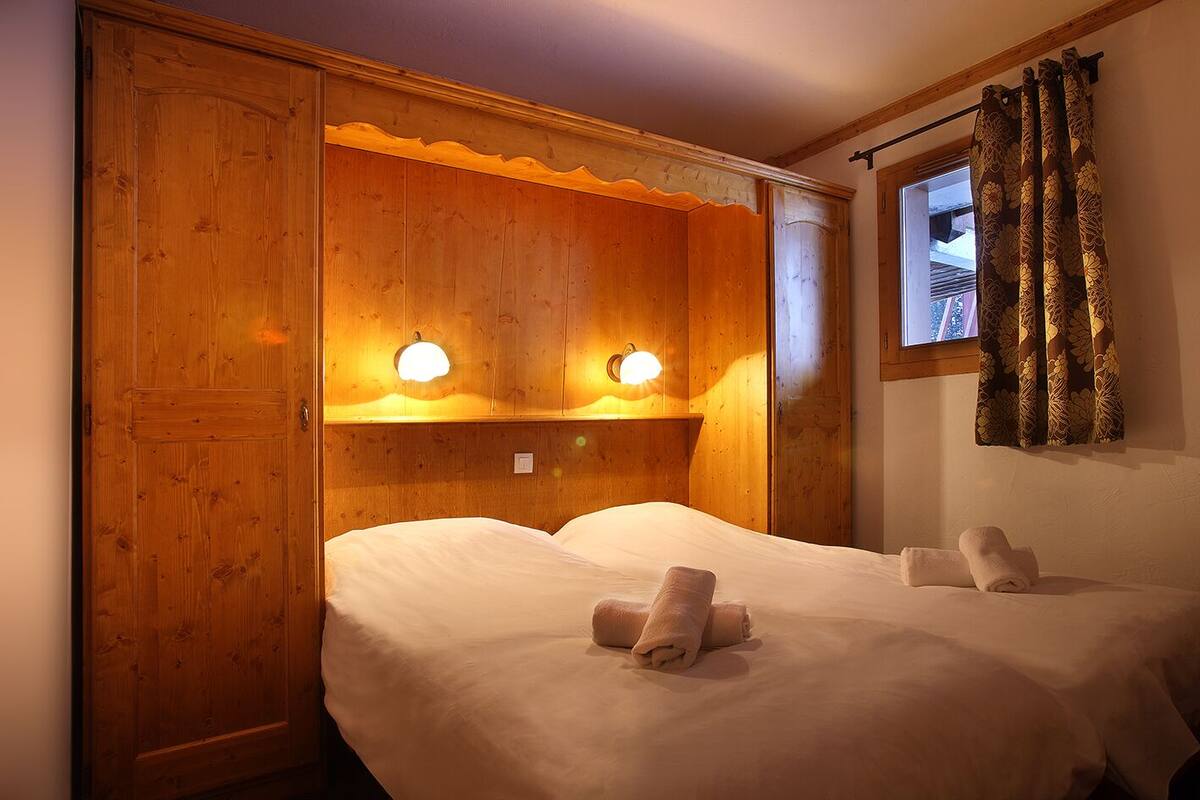Une pièce en bois avec deux lits, chacun doté d’une tête de lit, et deux lampes fixées au mur.
