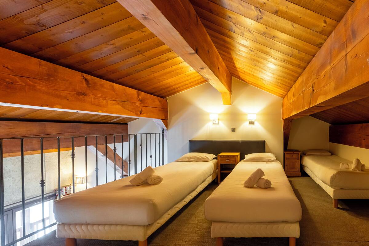 Une chambre avec des poutres en bois, deux lits simples avec des serviettes, une table de chevet et un escalier.