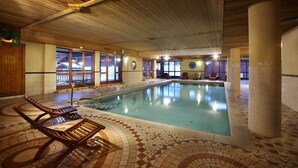 Une piscine intérieure à l’eau claire, dotée de chaises longues en bois et d’un sol carrelé.