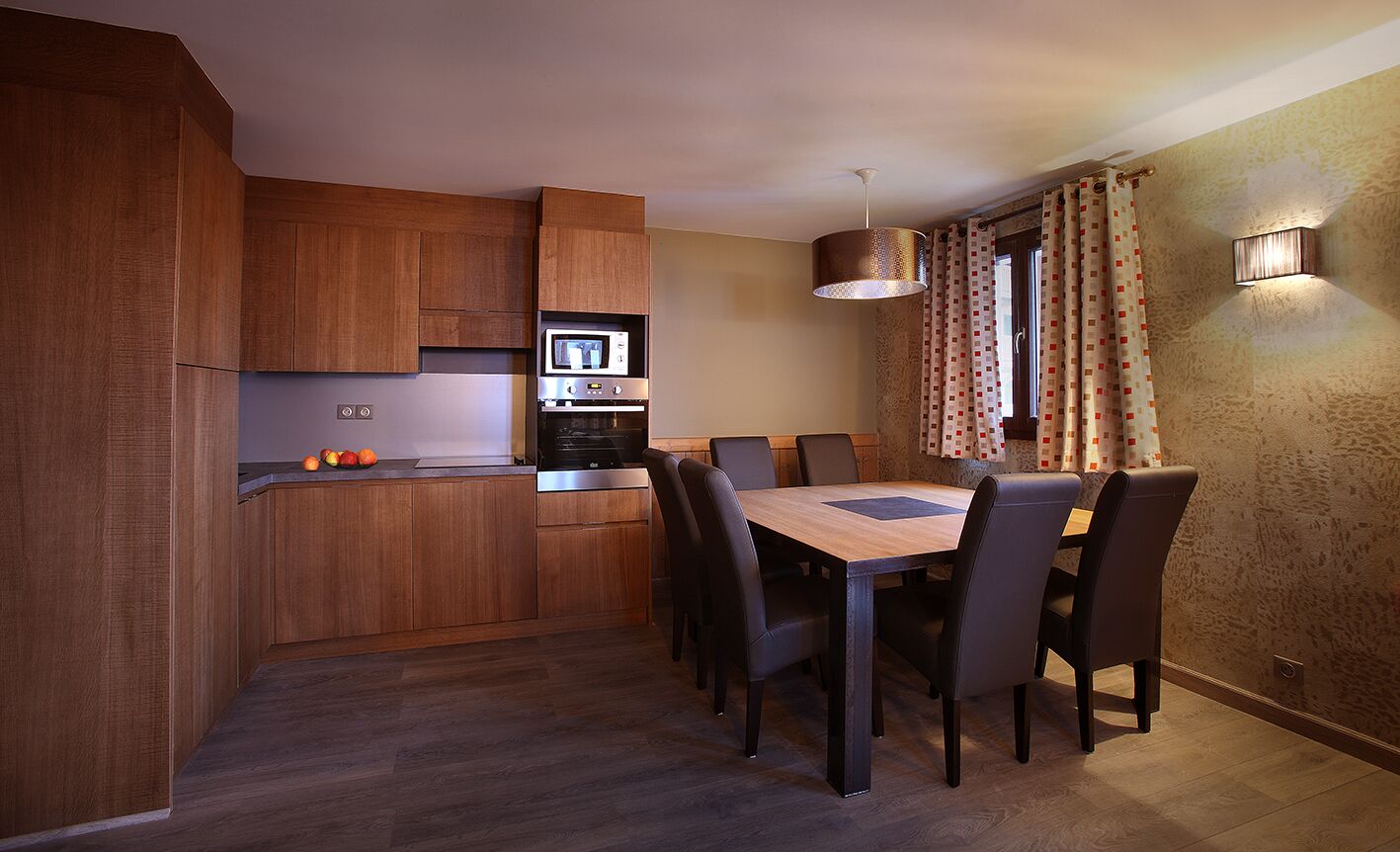 A modern kitchen with wooden cabinets, a built-in microwave, and a dining area with a wooden table and chairs.