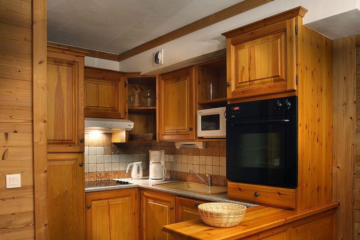 Une cuisine avec des meubles de rangement en bois, un four à micro-ondes, un four traditionnel, un évier et un sol carrelé en pierre.