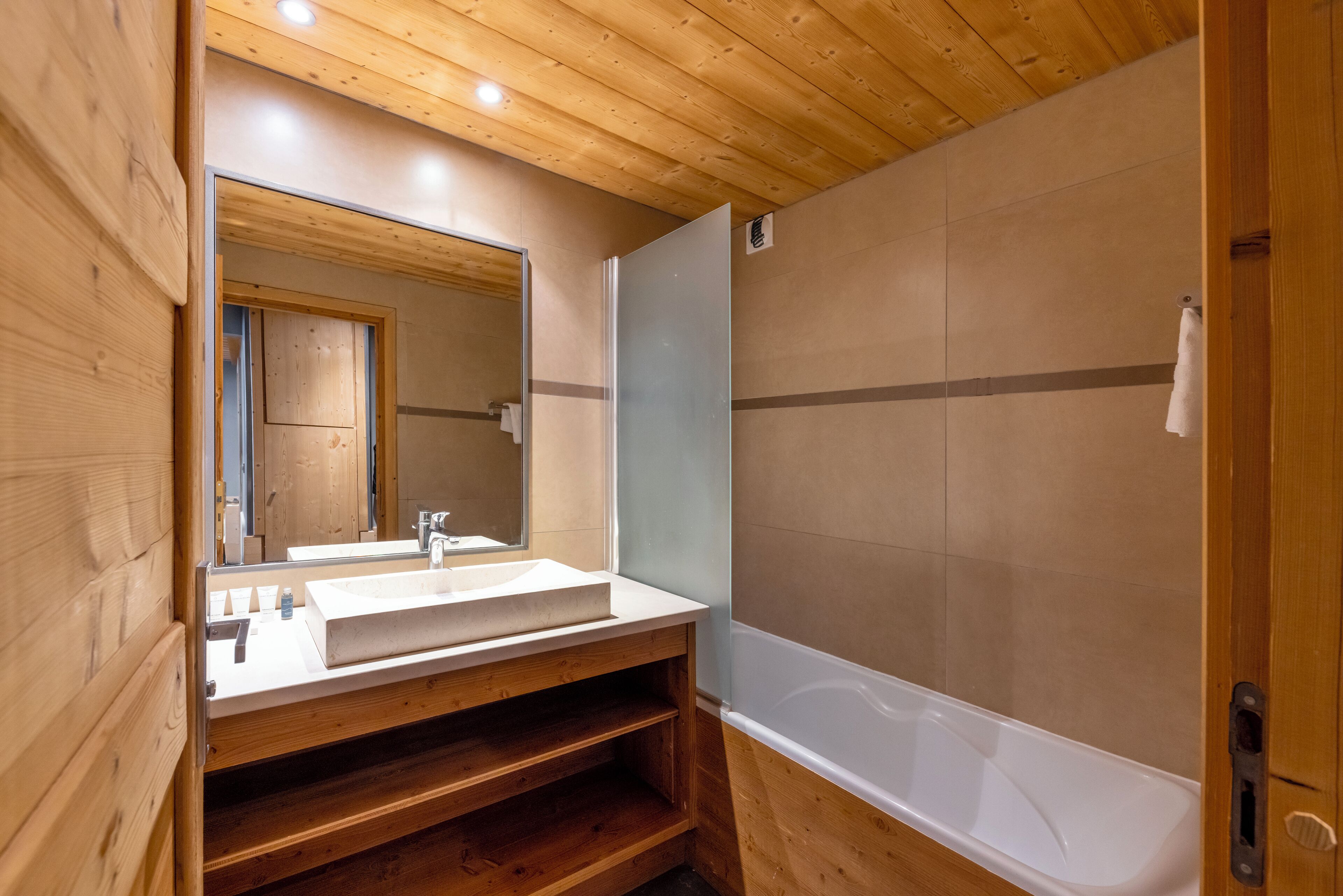 Une salle de bain aux murs lambrissés, dotée d’un grand miroir, d’un lavabo et d’une baignoire.
