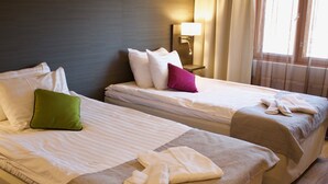 A hotel room with two beds, each with white linens and pillows, a nightstand with a lamp, and a window with curtains. - Hotel Kauppi (Tampere)