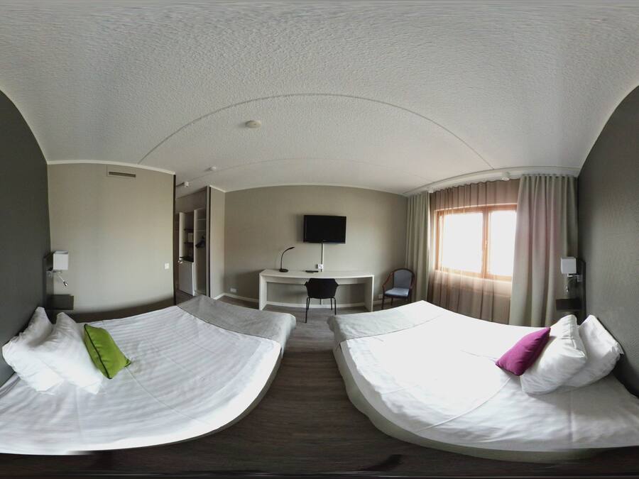 A hotel room with two beds, a desk, and a TV.