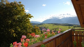 Un balc ón con vistas a un paisaje montañoso, barandilla de madera y plantas florecientes.