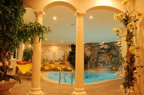 Un área de piscina interior con sillas reclinables amarillas, un mural de una pared de roca y plantas decorativas.
