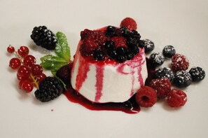 Un postre sobre una base blanca, rodeado de bayas y hojas de menta.