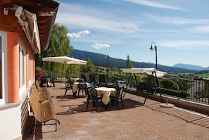 Une terrasse extérieure avec des tables et des chaises, un banc en bois et des parasols.