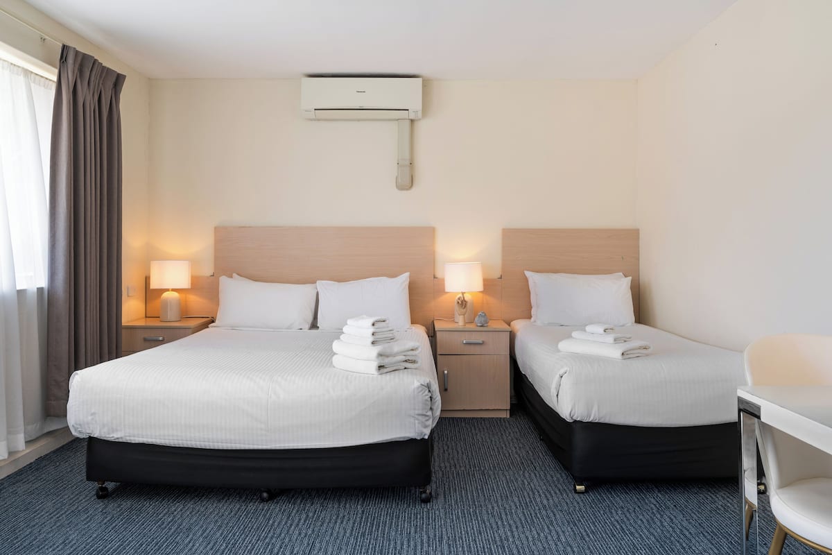 A hotel room with two beds, bedside lamps, a desk, and an air conditioning unit.