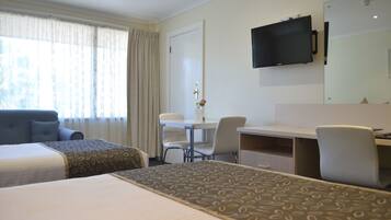 Une chambre d’hôtel avec deux lits, un bureau, une chaise, une télévision et une fenêtre avec des rideaux.