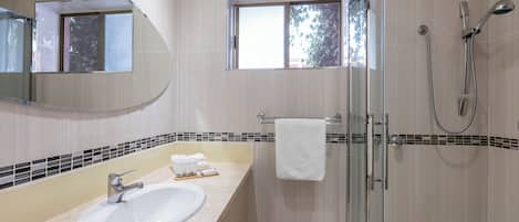 A bathroom with a sink, mirror, shower, and a window.