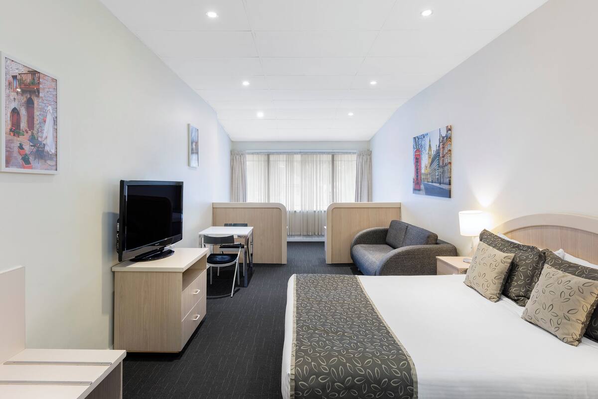A hotel room with a bed, a TV, a desk, and a chair.
