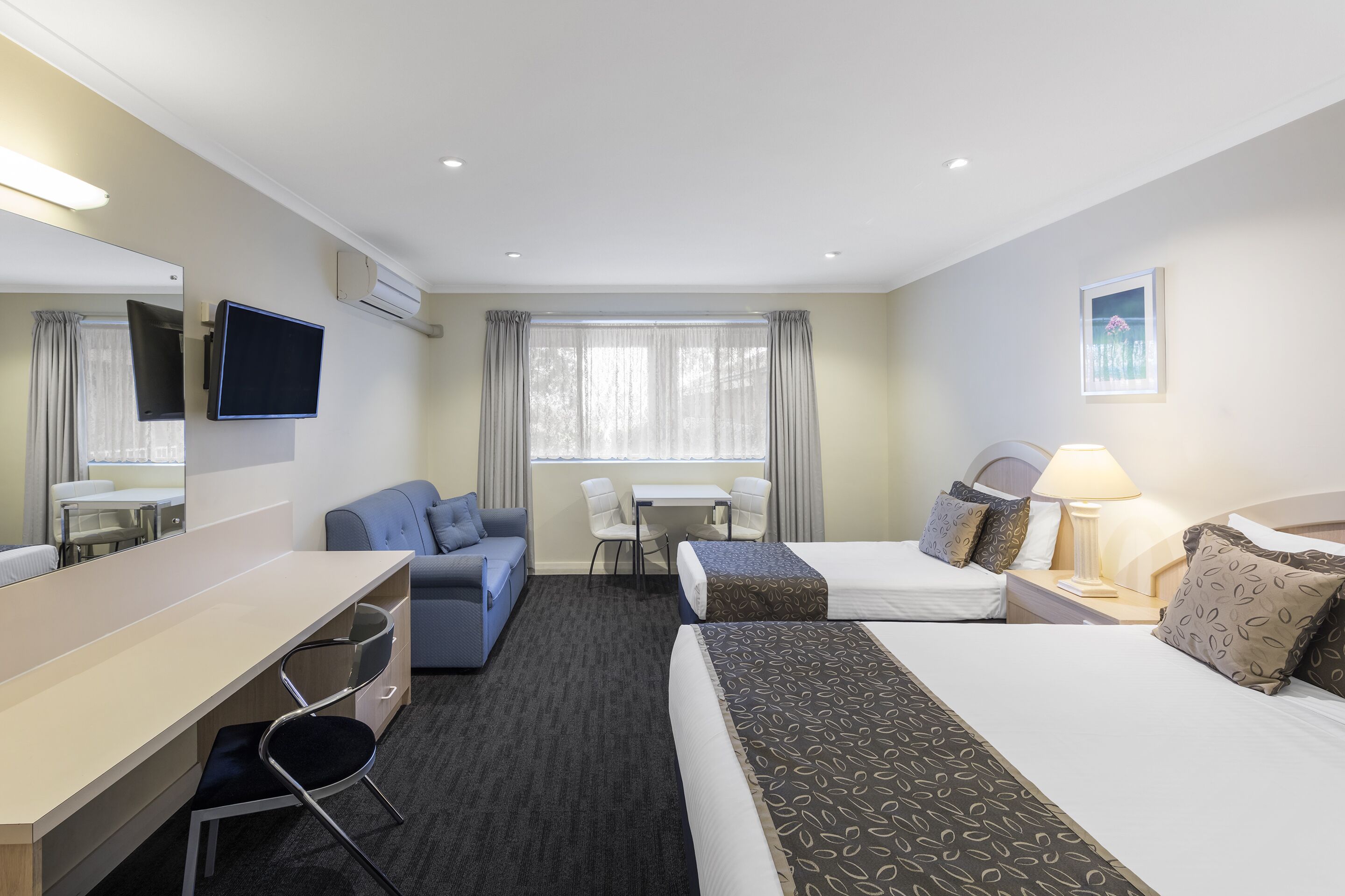 A hotel room with a bed, a desk, a chair, a sofa, a TV, and a window with curtains.