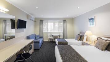Quarto de hotel com cama, escrivaninha, cadeira, sofá, televisão e janela com cortinas.