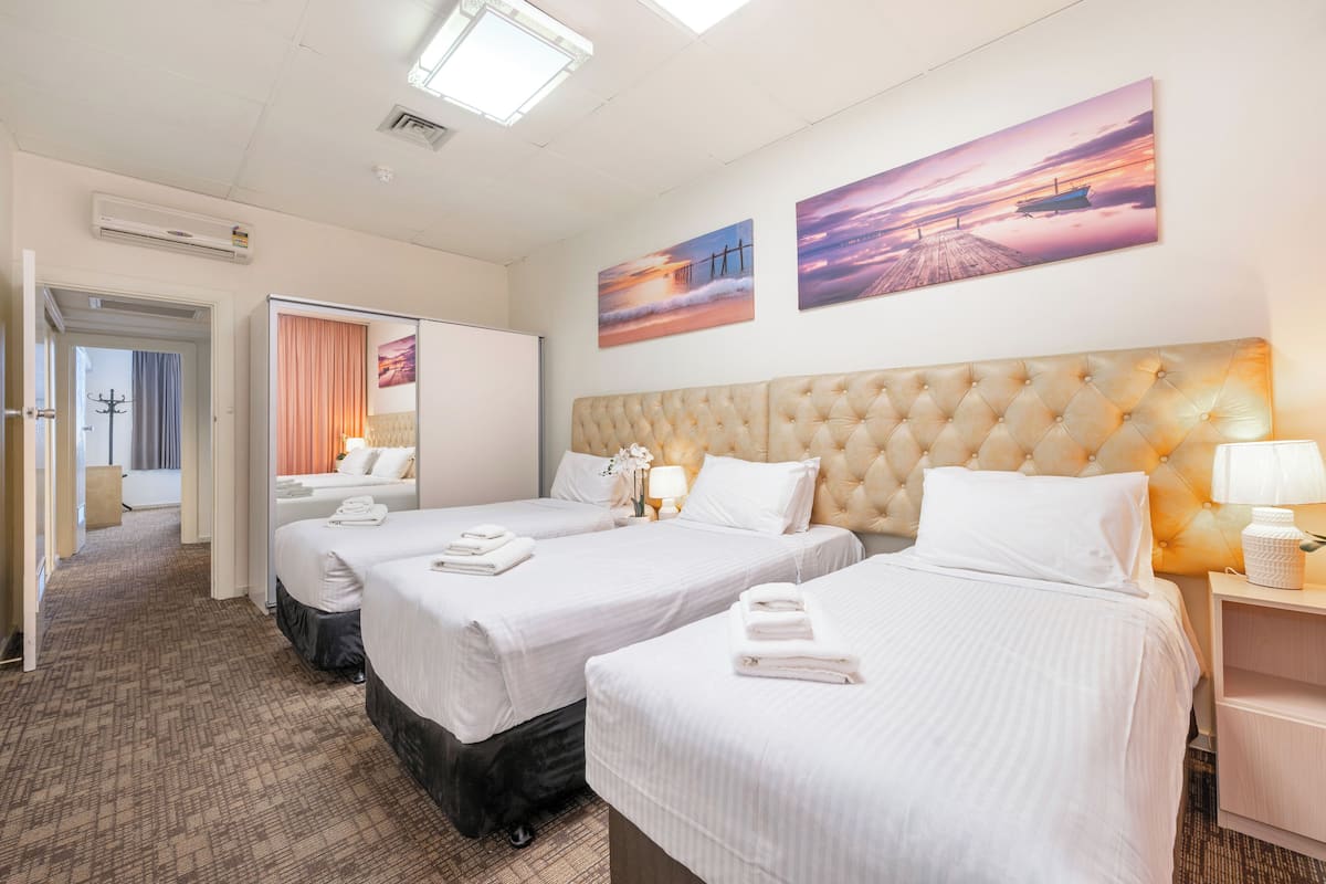 A hotel room with three beds, a large tufted headboard, and two wall-mounted paintings.