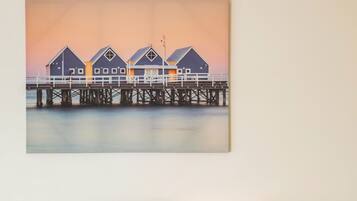 A hotel room with two beds, a nightstand with a lamp, and a painting of a pier.