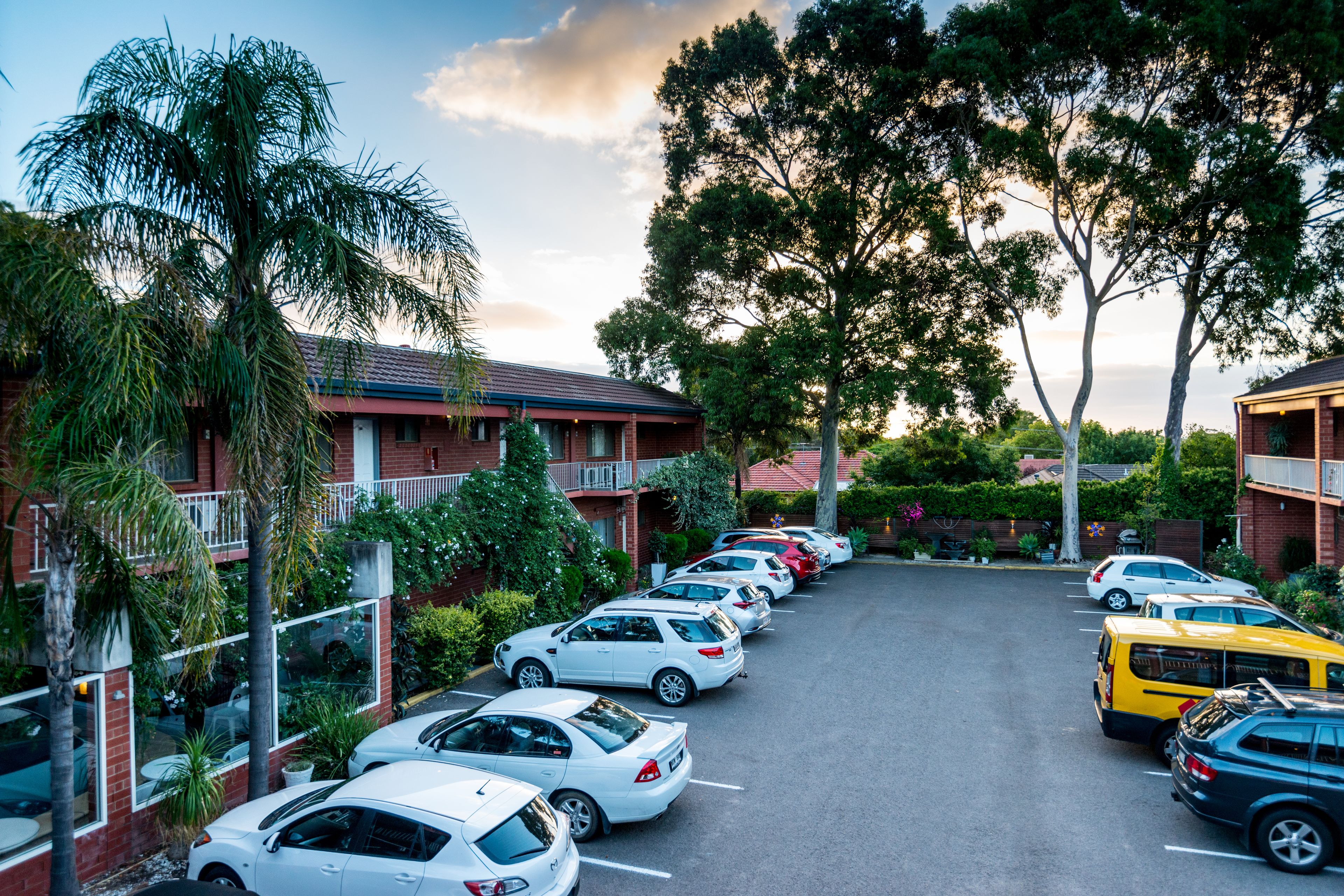 A parking lot with cars, a building with a red roof, and trees.