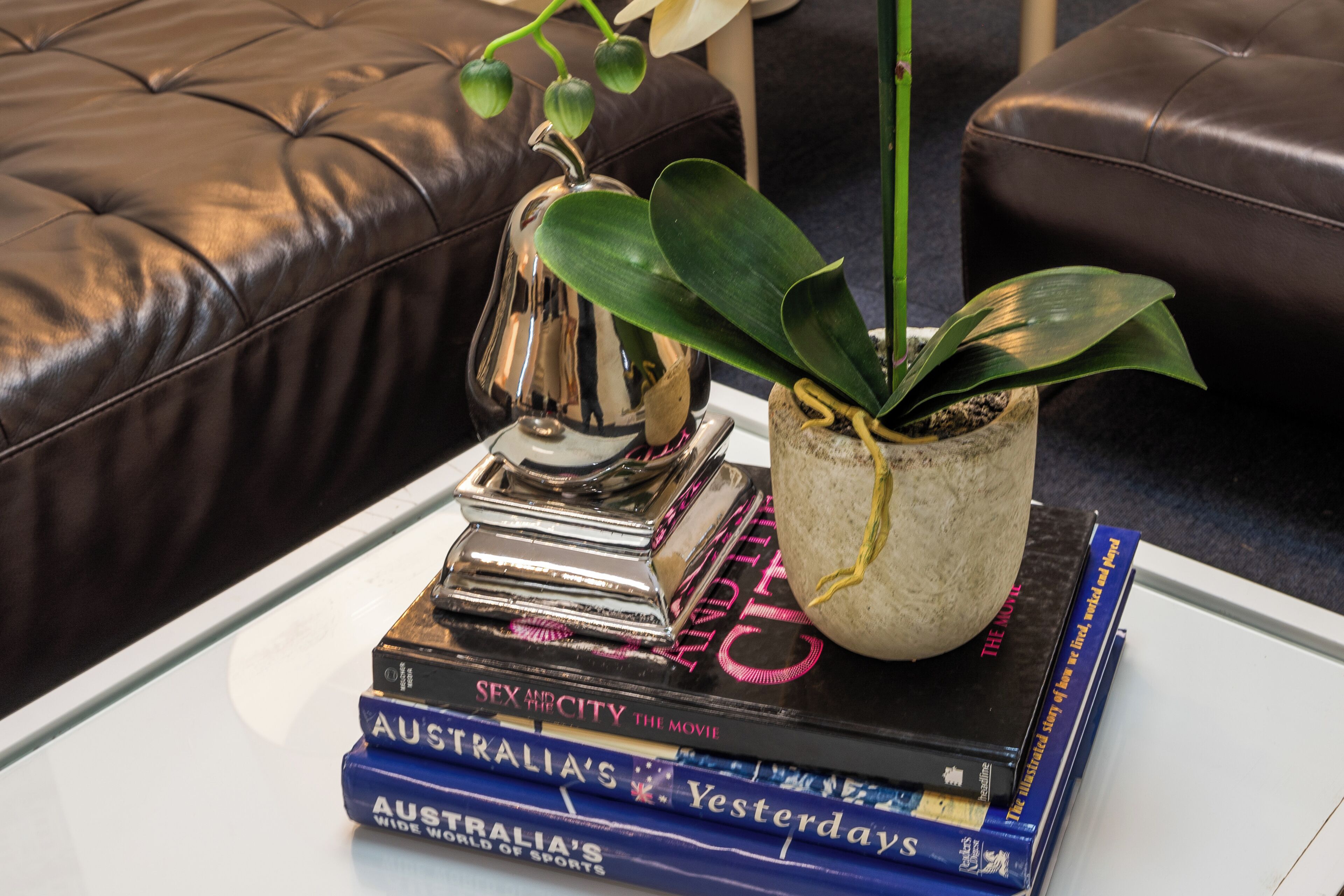 A stack of books on a white table with a potted plant and a decorative item.