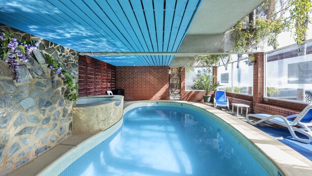 Una piscina interior con pared de piedra, cerca de madera y techo azul.