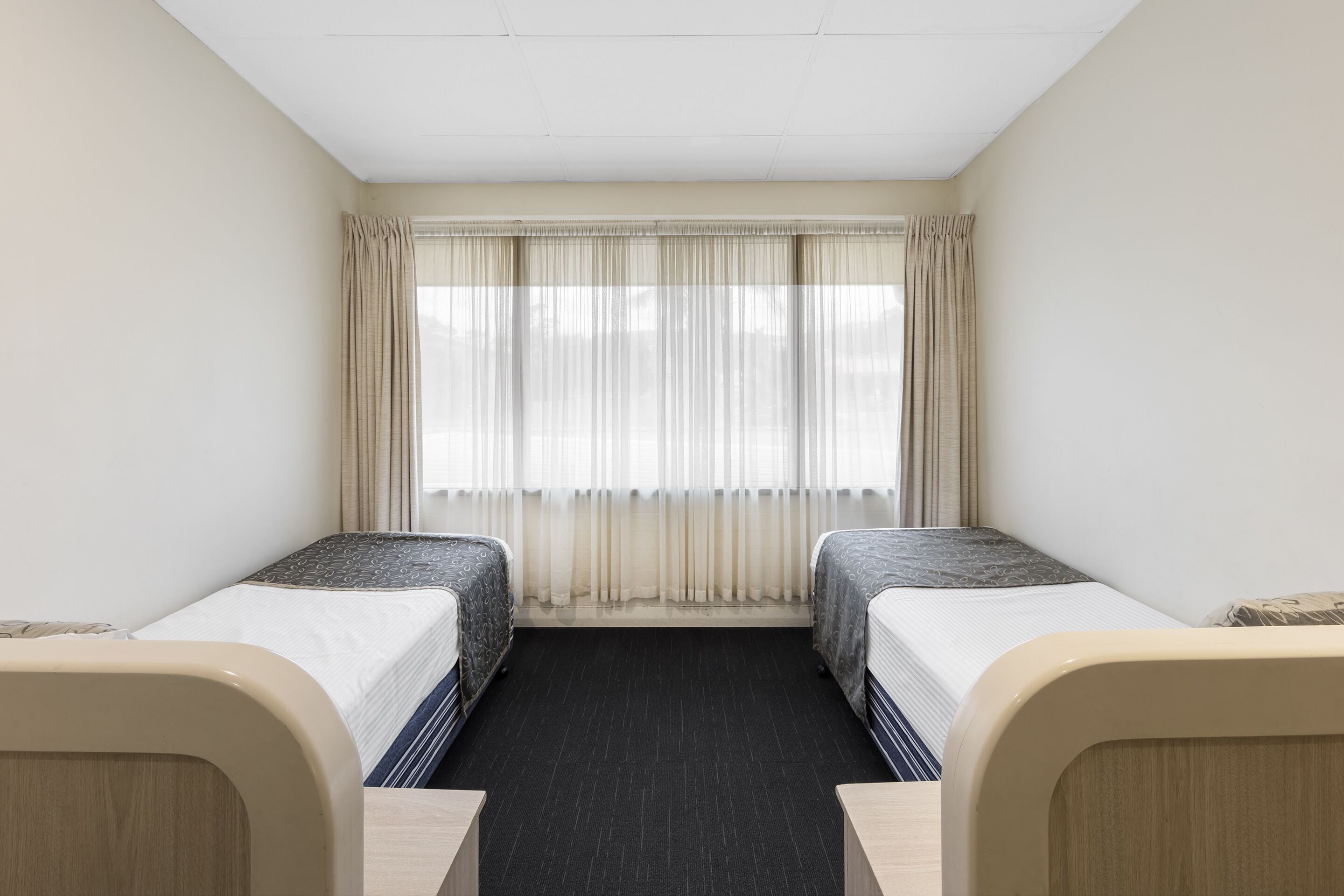 Una habitación de hotel con dos camas, un ventanal con cortinas y piso alfombrado.