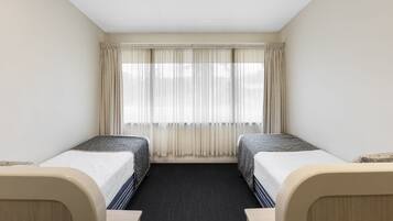 Una habitación de hotel con dos camas, un ventanal con cortinas y piso alfombrado.