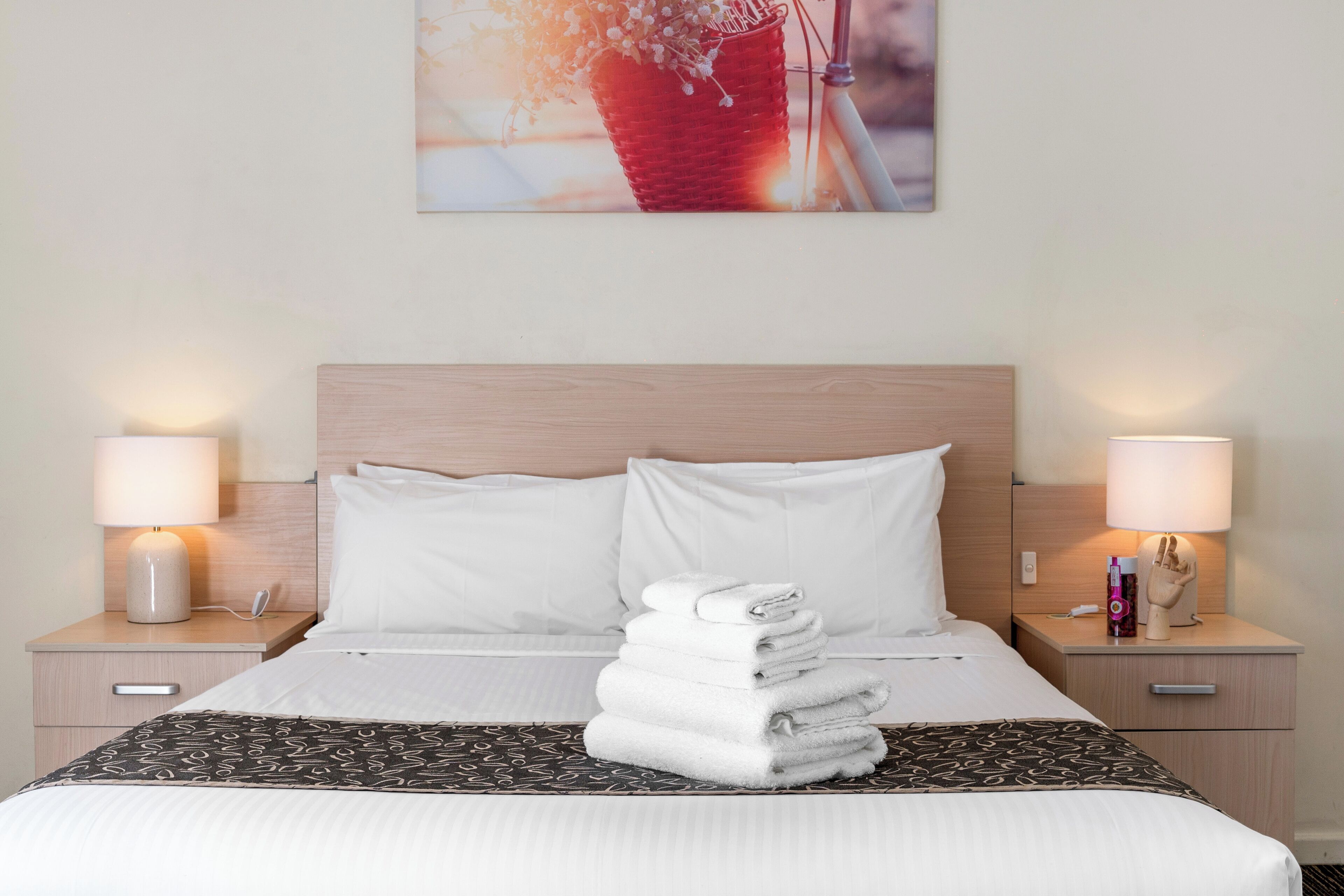 A neatly made bed with white linens, a stack of folded towels, and two bedside lamps on wooden nightstands.