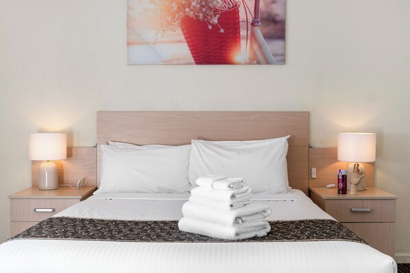 A neatly made bed with white linens, a stack of folded towels, and two bedside lamps on wooden nightstands. - Comfort Inn Burnside (Glenunga)