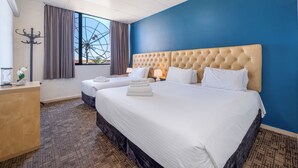 Una habitación de hotel con dos camas, un ventanal grande con cortinas, un adorno en la pared y un mostrador de recepción.