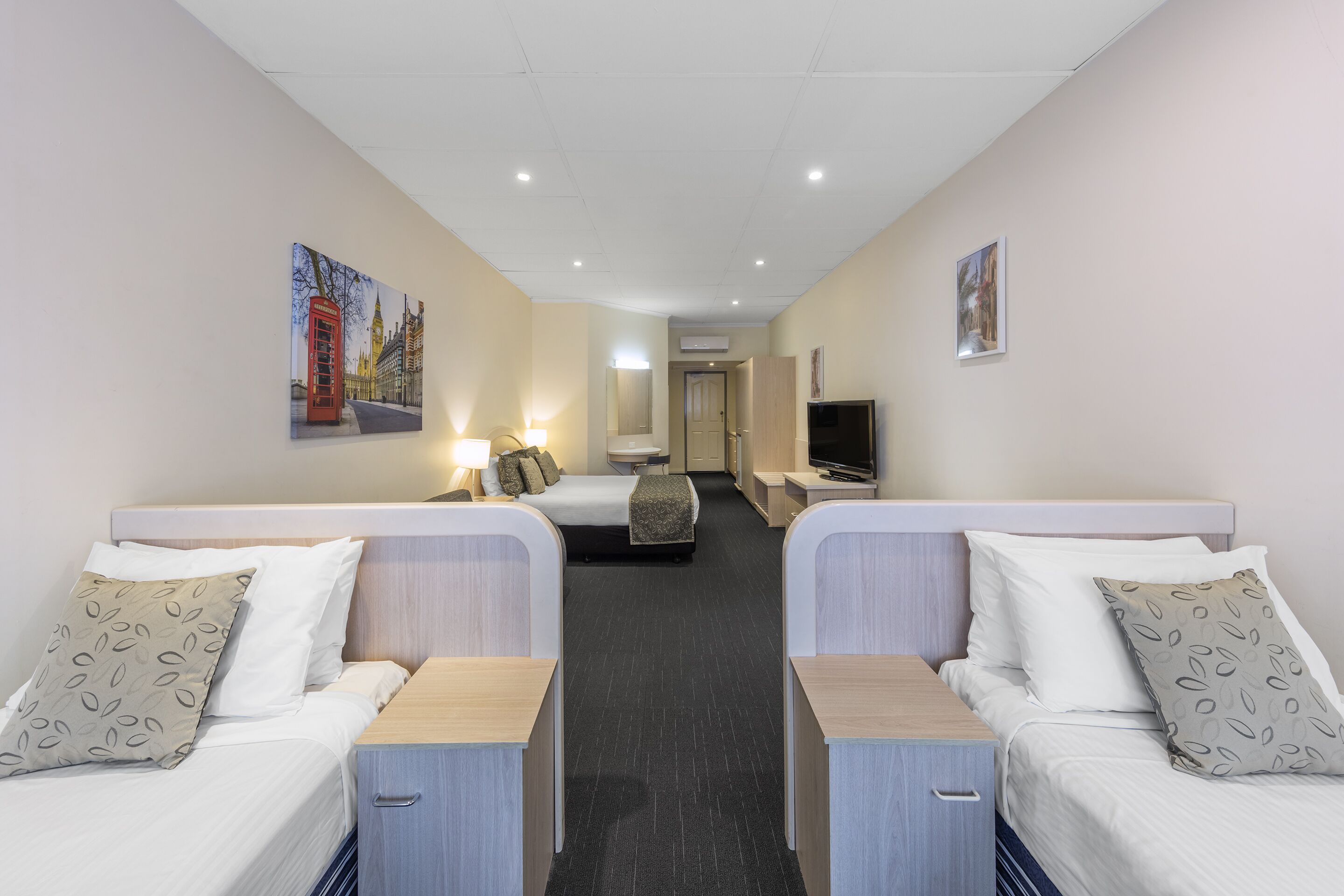 Ein Hotelzimmer mit zwei Betten, einem Fernseher, einem Schreibtisch und einem Bild an der Wand.