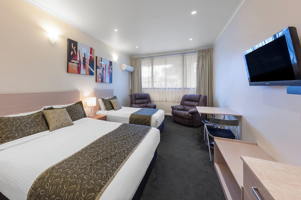 A hotel room with two beds, a desk, a chair, a TV, and artwork on the wall.