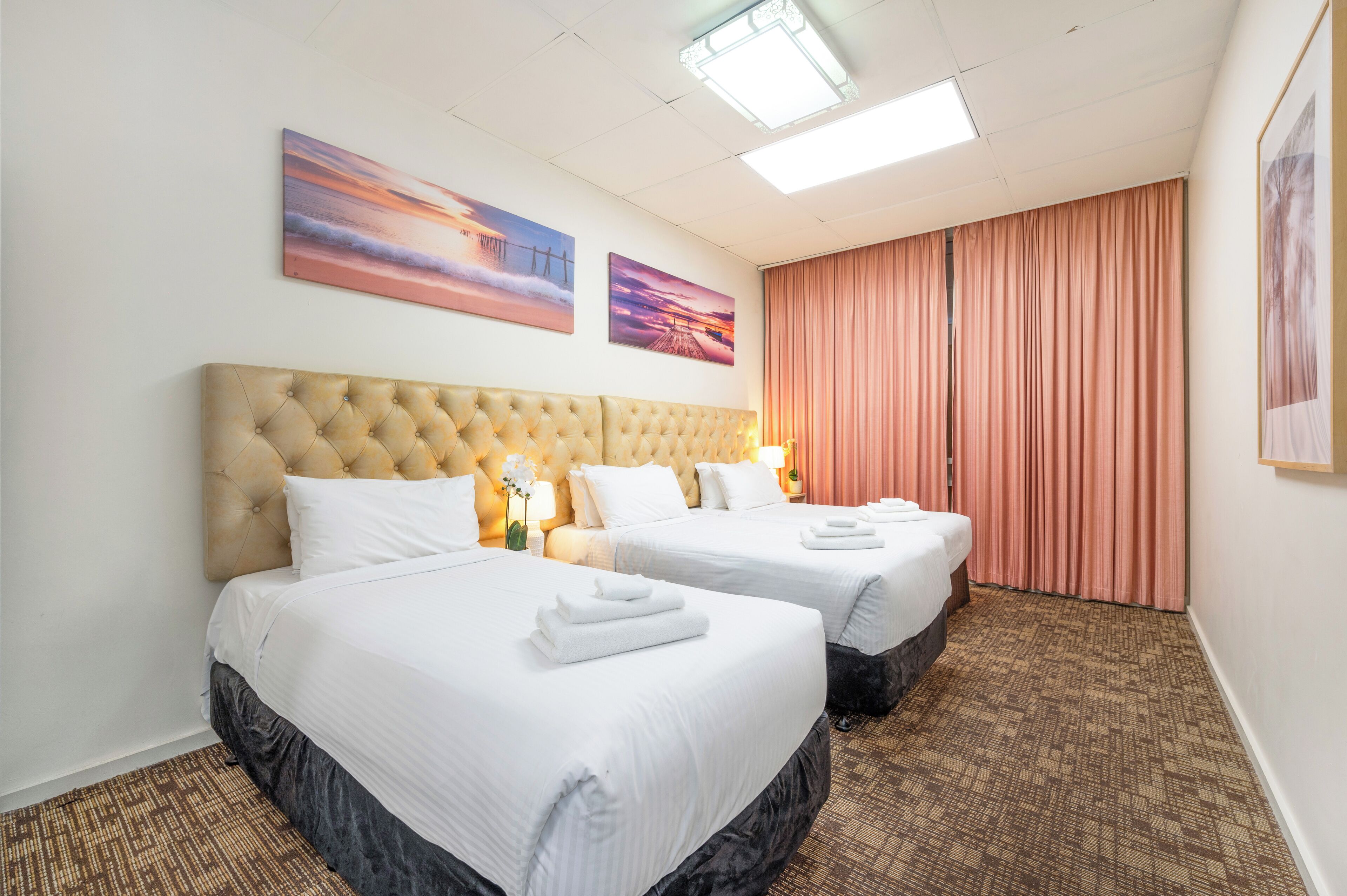 A hotel room with two beds, a large tufted headboard, and a view of the city.