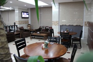 A modern dining area with a round wooden table, several chairs, a sofa, and a television mounted on the wall.