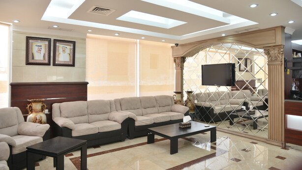 A modern living room with a sectional sofa, a coffee table, and a TV mounted on the wall. - Al Muhanna Plaza Hotel (Salmiya)