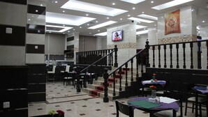 A hotel lobby with a staircase, seating areas, and a TV mounted on the wall. - Al Muhanna Plaza Hotel (Salmiya)