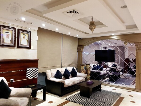 Un salon moderne avec un canapé, un fauteuil, une table basse et un téléviseur. Des tableaux encadrés ornent le mur, et une lampe décorative complète l’ensemble.
