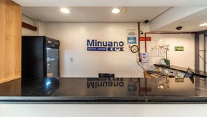 A reception area with a black counter, a clock, a plant, and a sign for 'Minuano Hotel Home.' - Hotel Minuano Home (Porto Alegre)