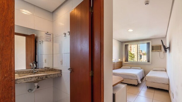 A hotel room with a bathroom, a bed, a desk, and a window. - Hotel Minuano Home (Porto Alegre)