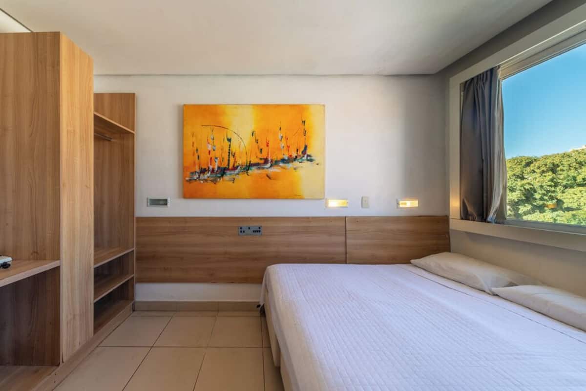 Een hotelkamer met een bed, een houten kast, een schilderij aan de muur en een raam met uitzicht.
