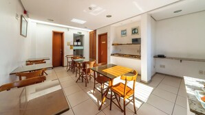 A dining area with multiple tables and chairs, a kitchen area with a counter and shelves, and a visible exit door. - Hotel Minuano Home (Porto Alegre)