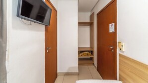 A hallway with a TV mounted on the wall, wooden doors, a closet with shelves, and a bed with a wooden headboard. - Hotel Minuano Home (Porto Alegre)