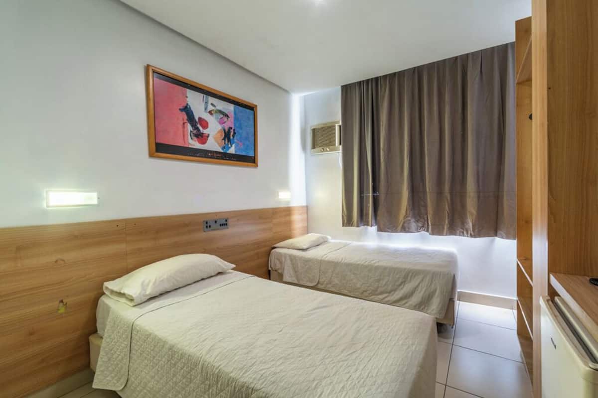 Een hotelkamer met twee bedden, een schilderij aan de muur, een raam met gordijnen en een houten hoofdbord.