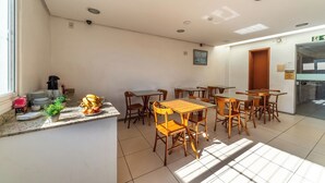 A dining area with tables and chairs, a kitchen counter with dishes and a plant, and a door leading to another room. - Hotel Minuano Home (Porto Alegre)