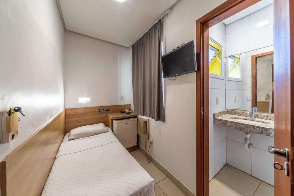 Hotelkamer met een bed, een televisie, een klein bureau, een verwarming en een badkamer met een wastafel en spiegel.